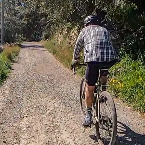 A person in casual clothing rides a bicycle on a gravel path.