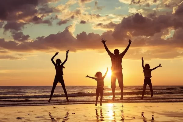 Persone che saltano sulla spiaggia durante un tramonto.