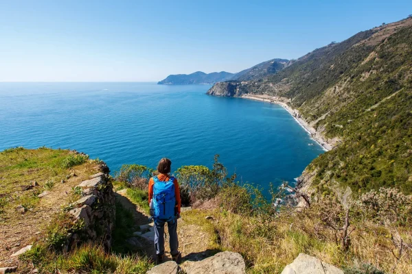 Escursionista con zaino guarda un panorama costiero mozzafiato.